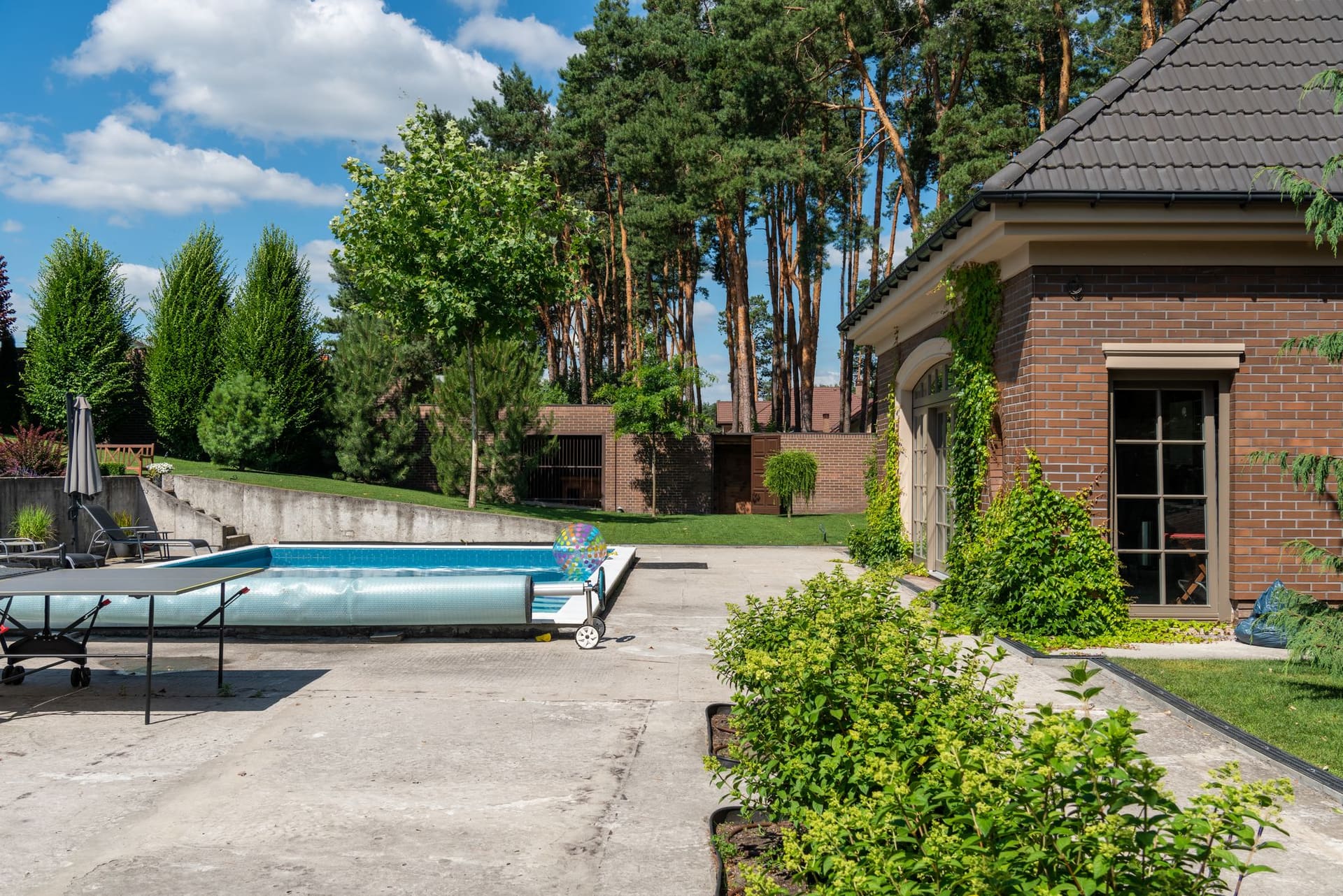 Backyard pool with a retractable cover rolled along one end, beside a brick house