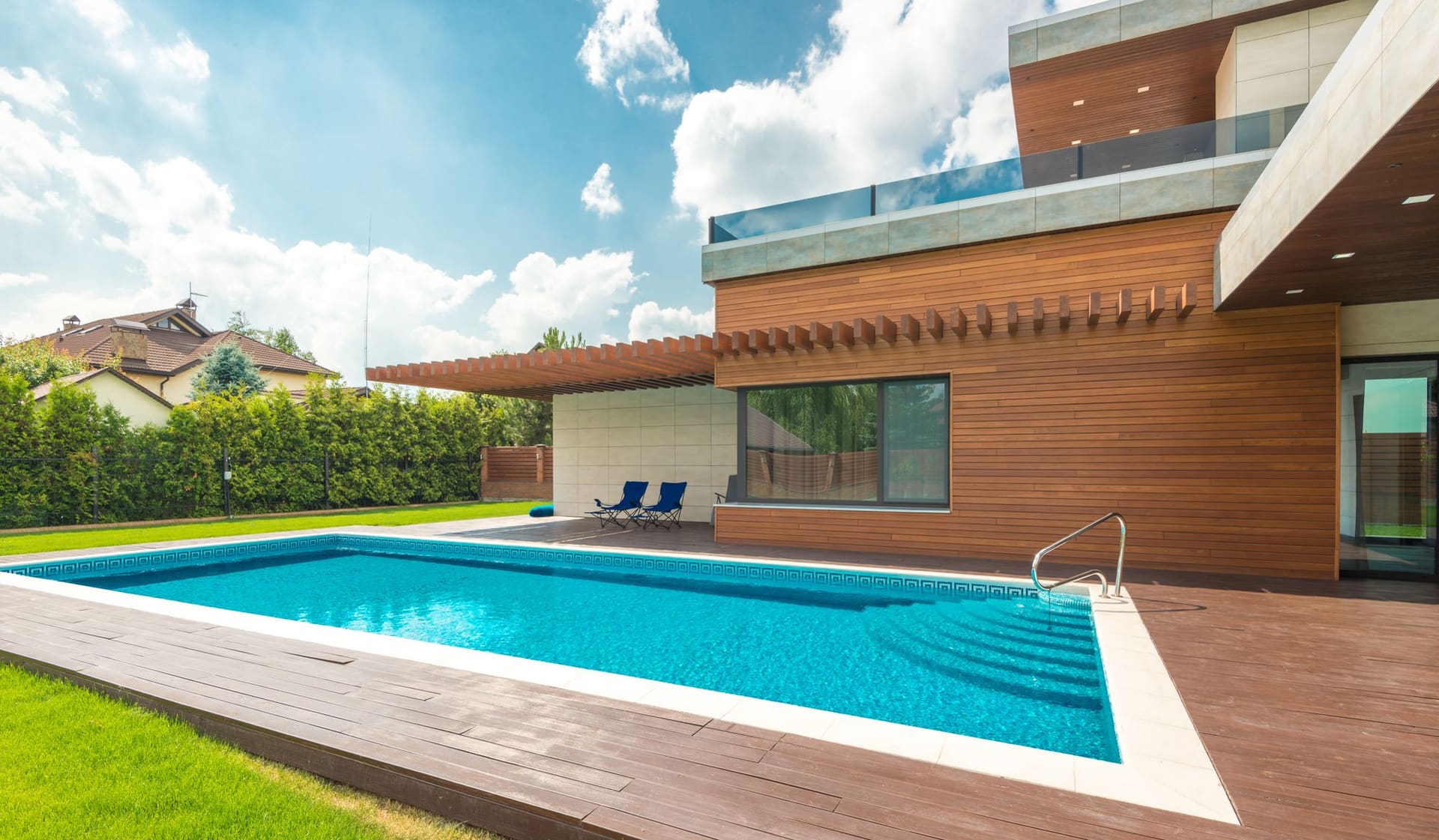Backyard swimming pool beside a modern house under a blue sky