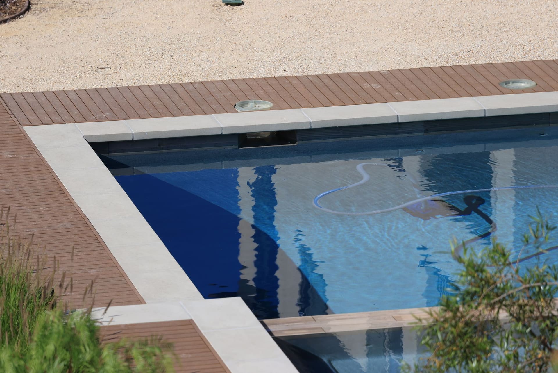 Clear pool with wooden decking and a pool hose along the edge